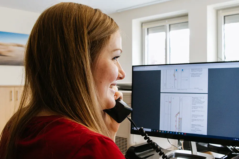 Mitarbeiterin der Disposition am Telefon vor einem Bildschirm mit Planunterlagen