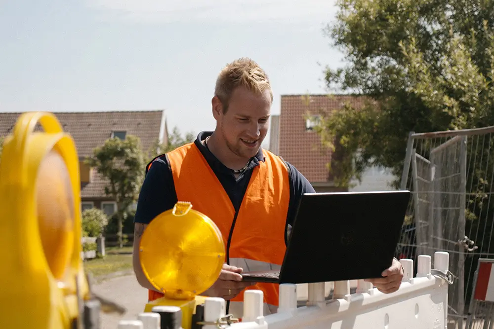 Bauleiter mit Laptop an einer Baustellenabsperrung